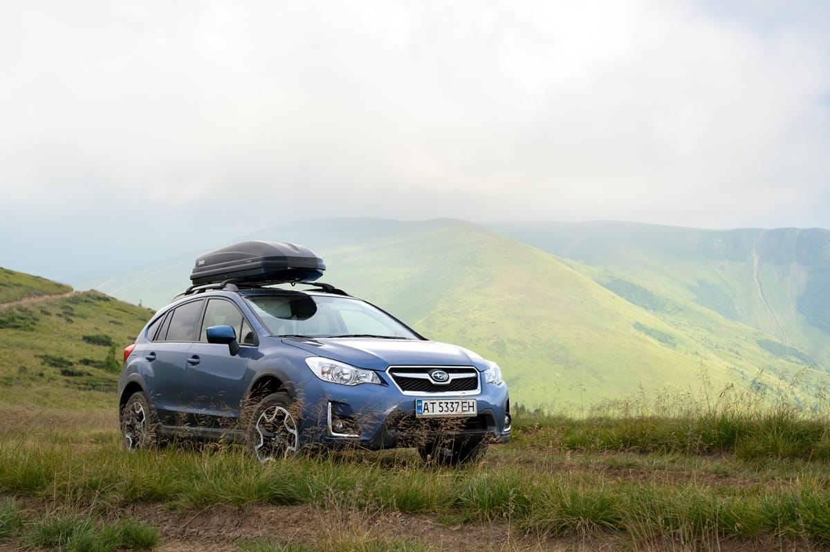Blue Subaru Crosstrek navigating a rugged off-road trail surrounded by dry, rocky terrain and distant mountains under a clear sky