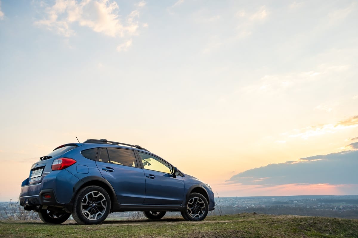 Blue off-road SUV parked on a rugged landscape at sunset, with golden light casting dramatic shadows over the terrain and distant hills