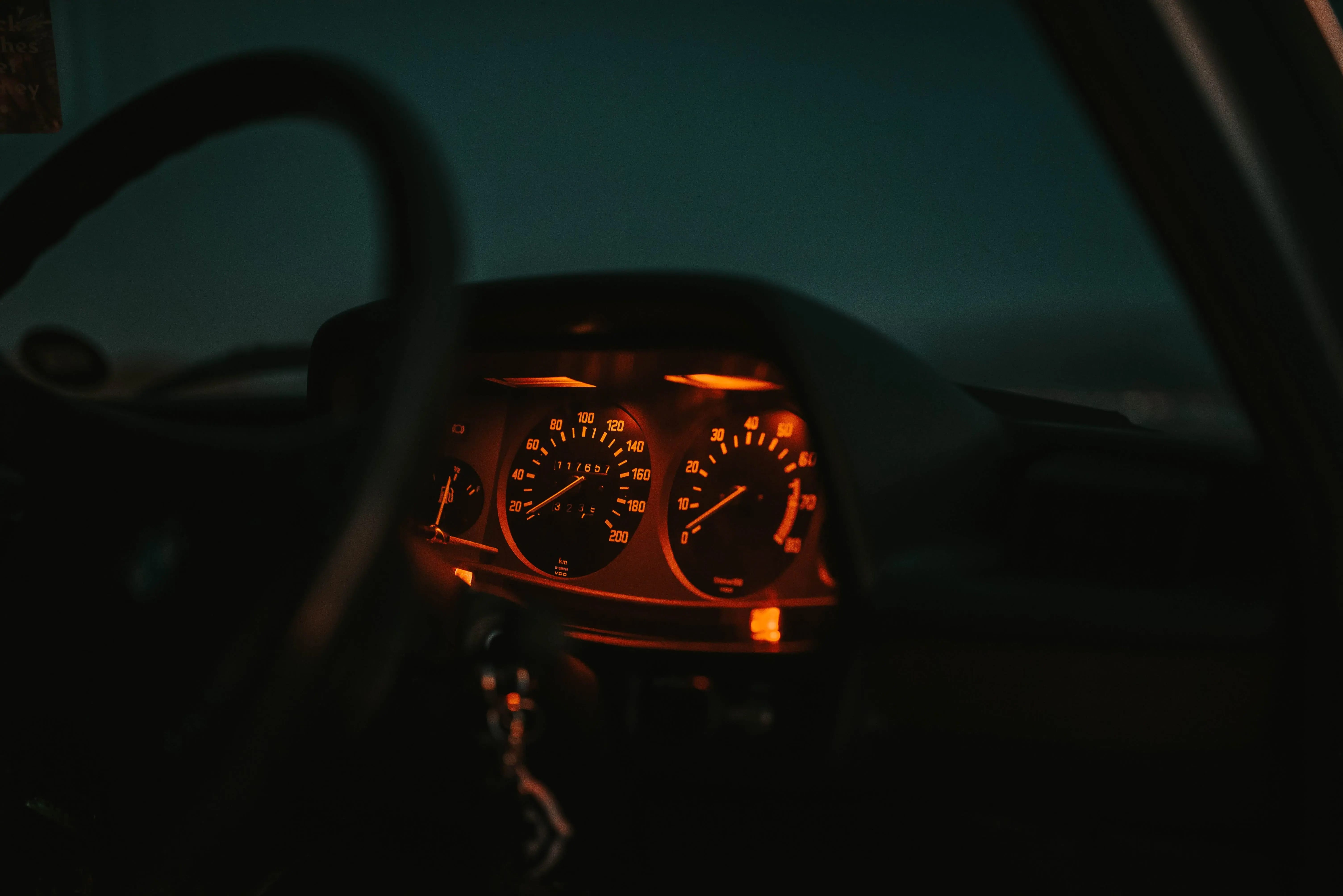 Close-up of a classic car dashboard illuminated at night, showing an analog speedometer, tachometer, and fuel gauges with orange backlighting