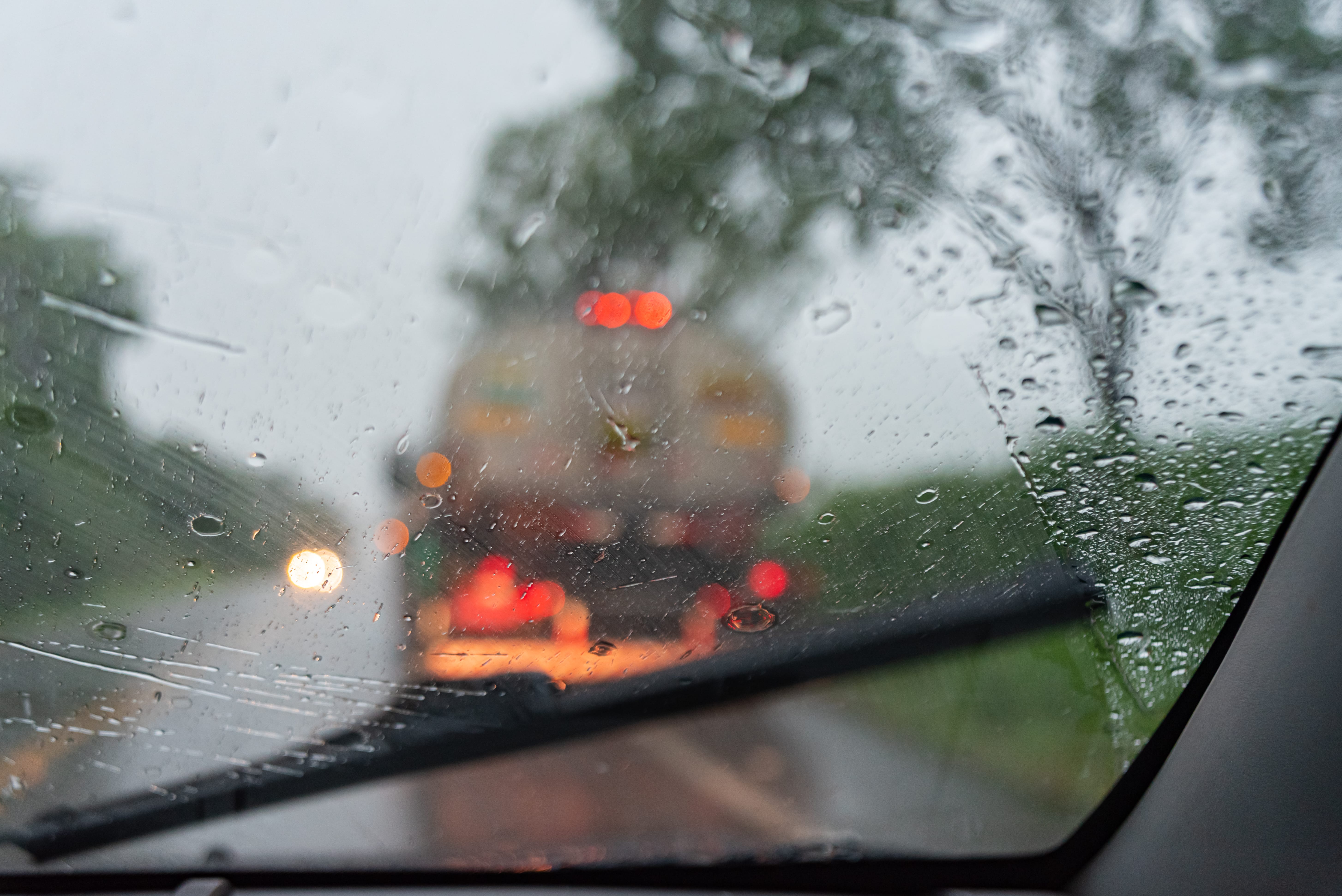 View through a car windscreen during heavy rain, with water droplets and a wiper in motion