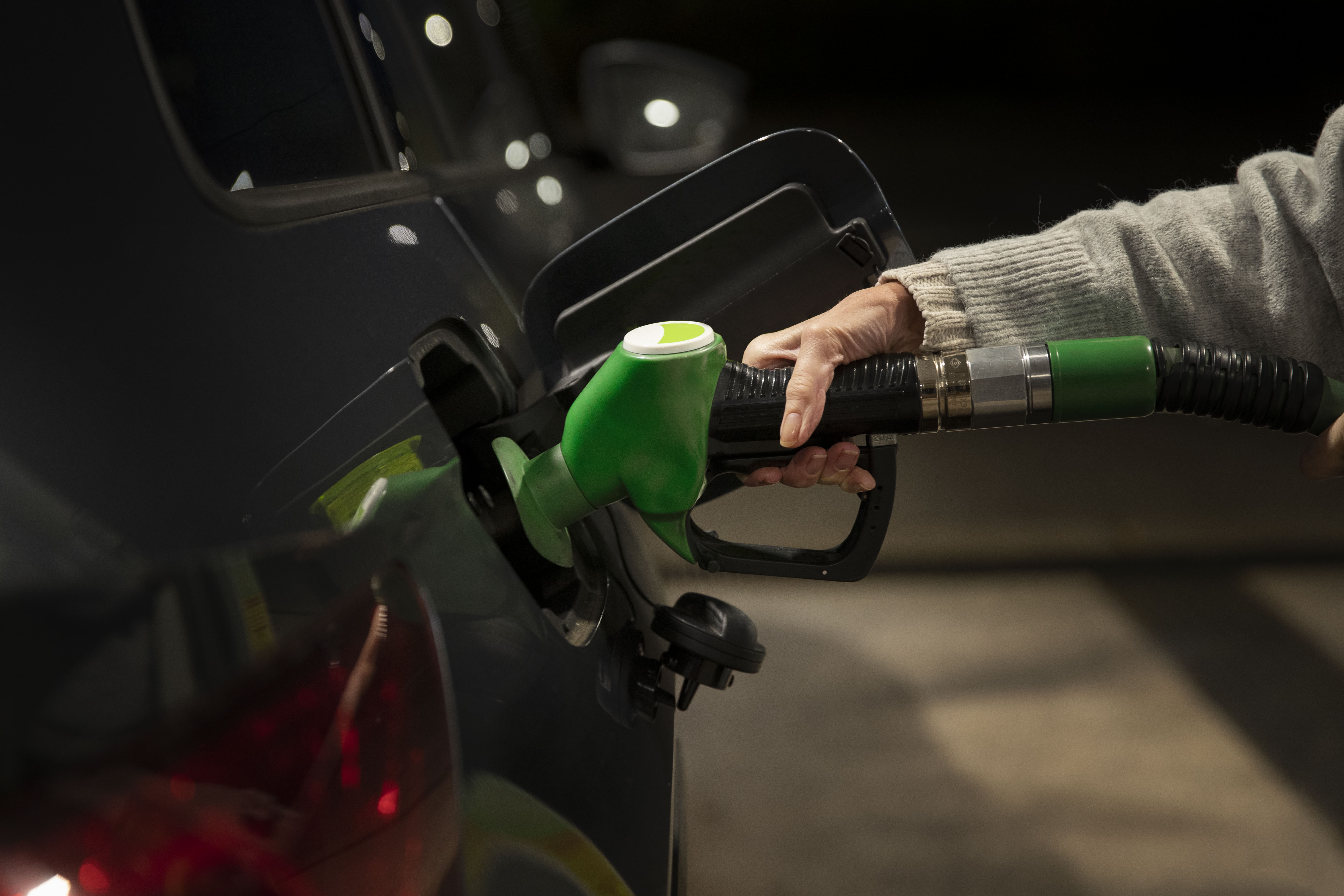 Close-up of a person refuelling a dark-coloured car at a petrol station