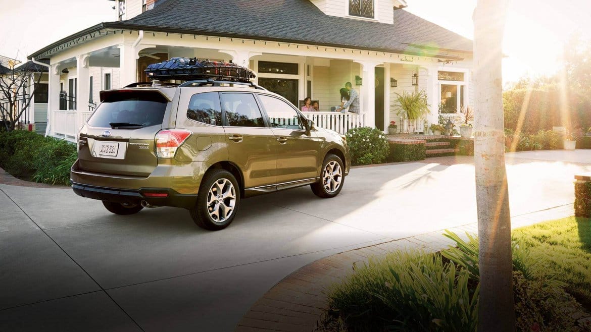 bronze Subaru Forester parked in the driveway of a modern suburban home at sunset.