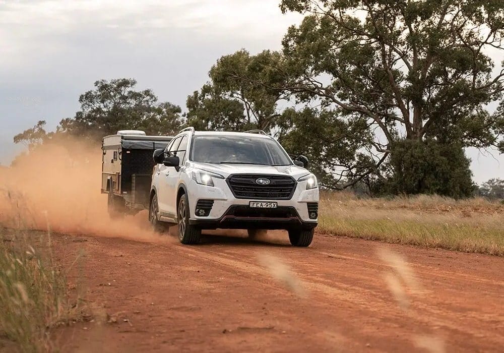 white Subaru Forester towing a camper trailer along a dusty red dirt road in the Australian outback