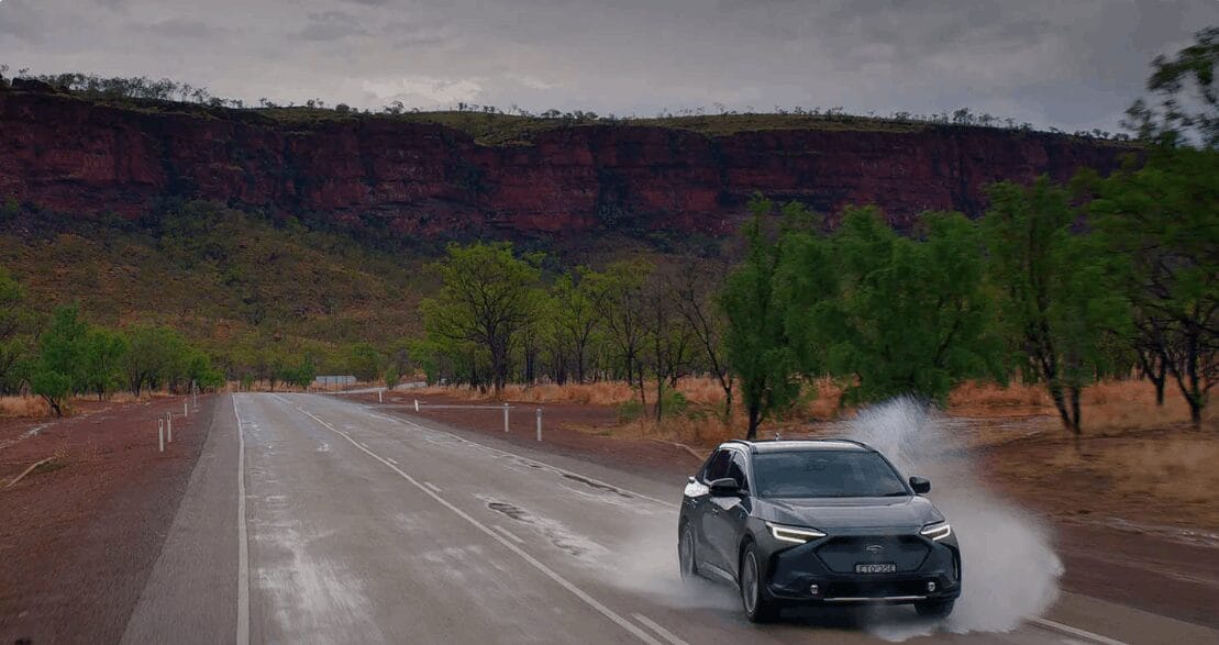 Subaru Solterra in motion on a rain-soaked road through a rugged landscape.
