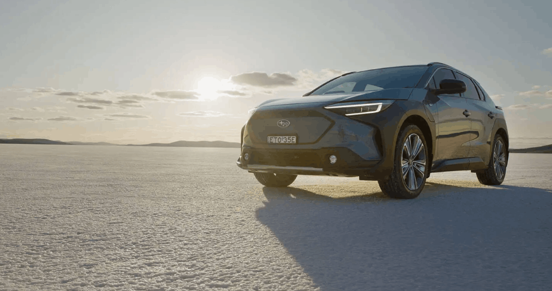 Subaru Solterra on an open salt plain with the sun setting behind it