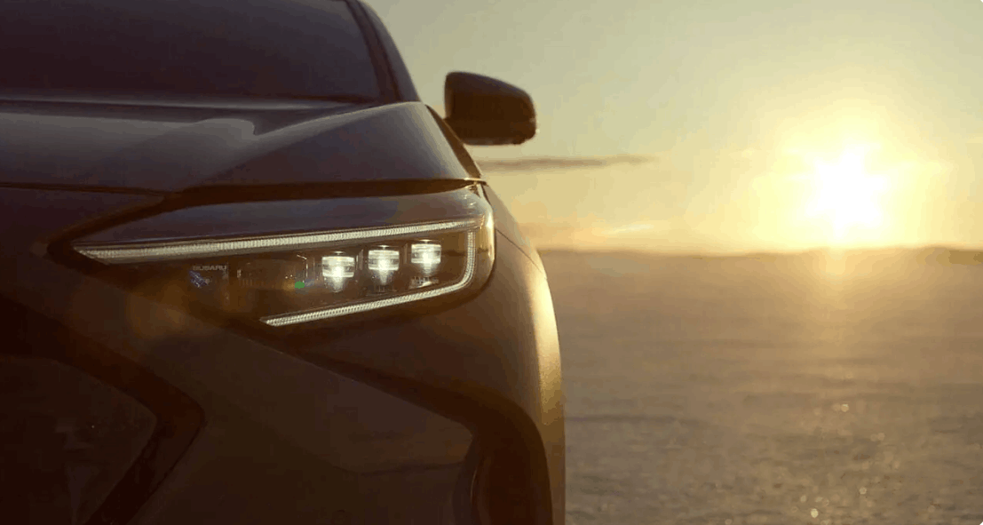 Close-up of Subaru front headlight illuminated at sunset with warm light in the background