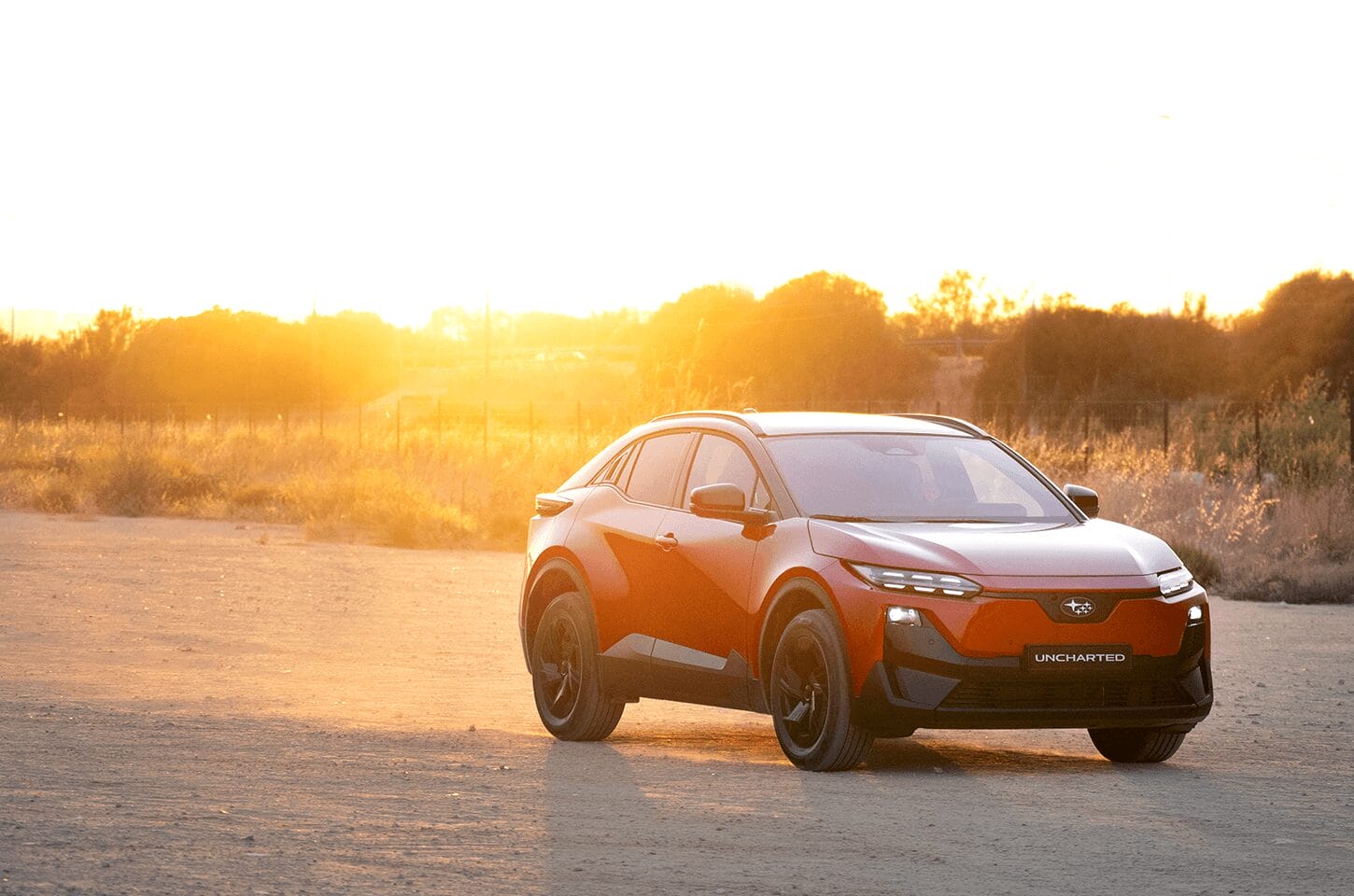 Red Subaru Uncharted parked on a gravel road at sunset with warm golden light in the background.