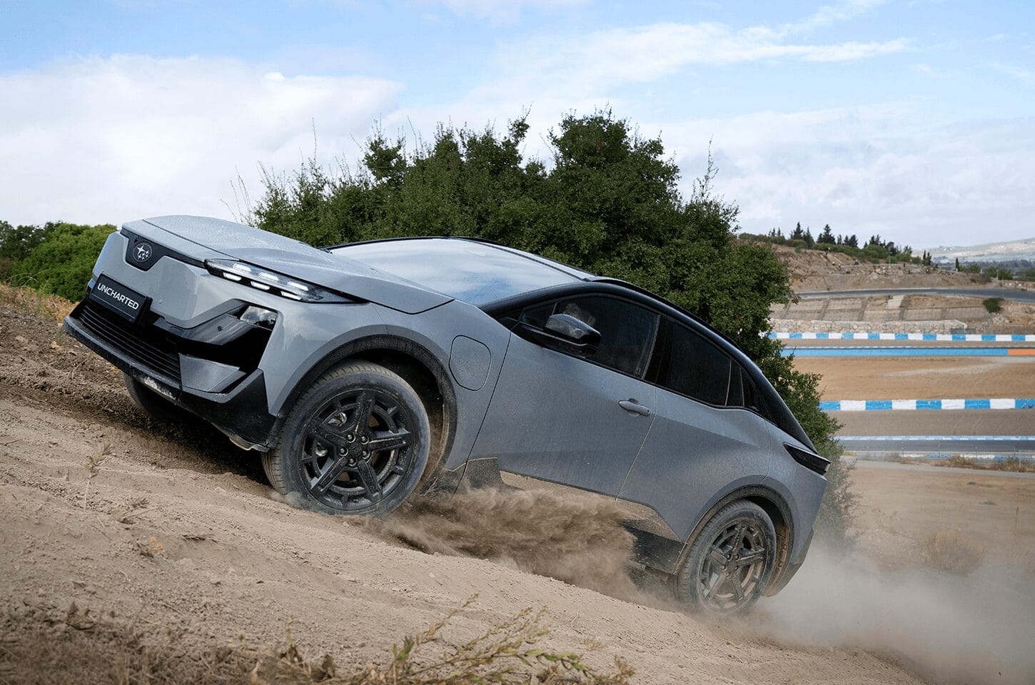 Grey Subaru Uncharted climbing a dirt incline with dust surrounding the vehicle during off-road driving.