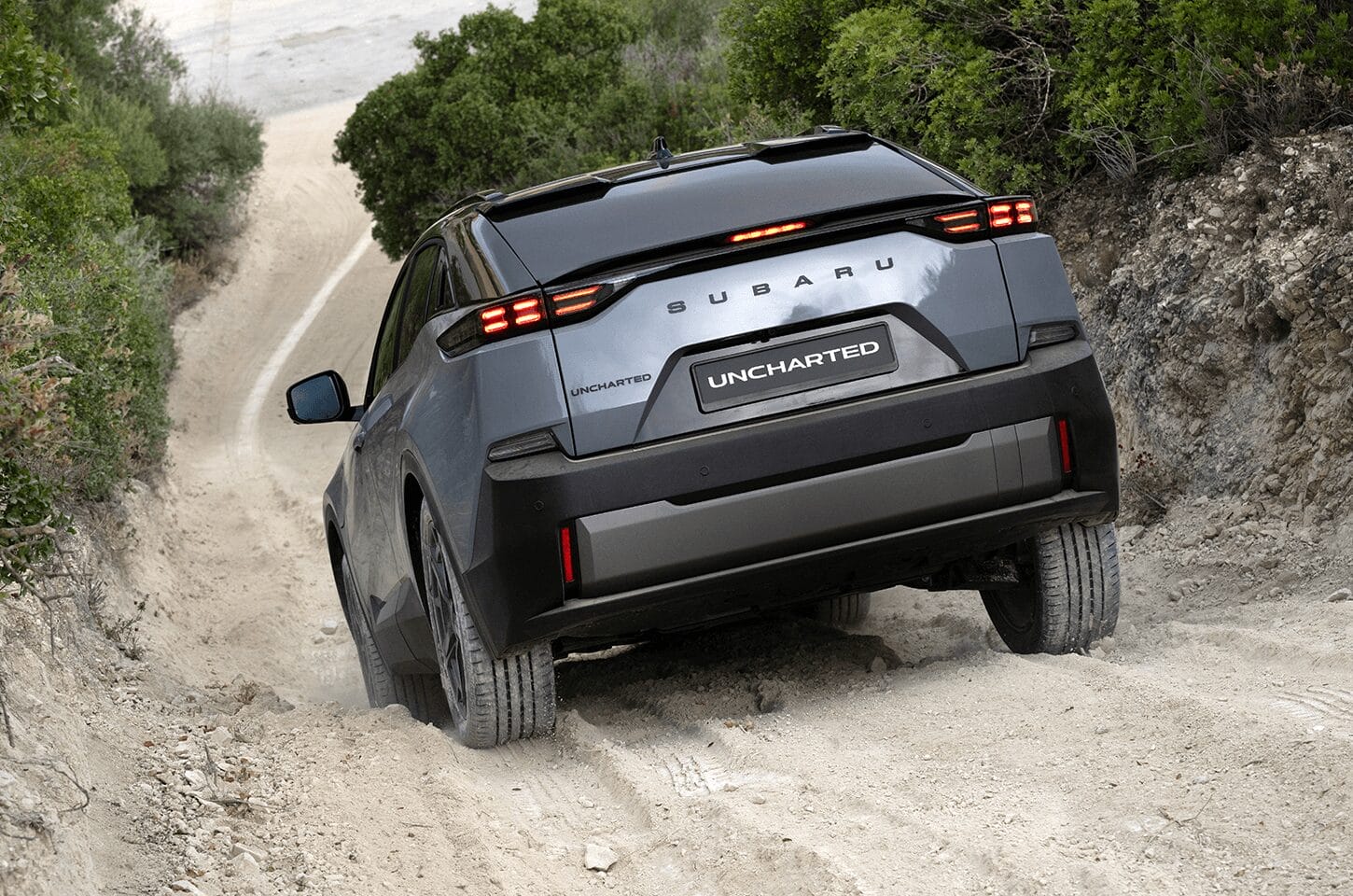 Rear view of the Subaru Uncharted driving along a rugged off-road track with illuminated LED tail lights.