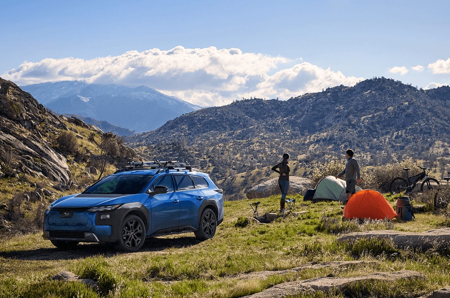 Subaru Trailseeker parked at a campsite in the mountains beside tents and bicycles.]