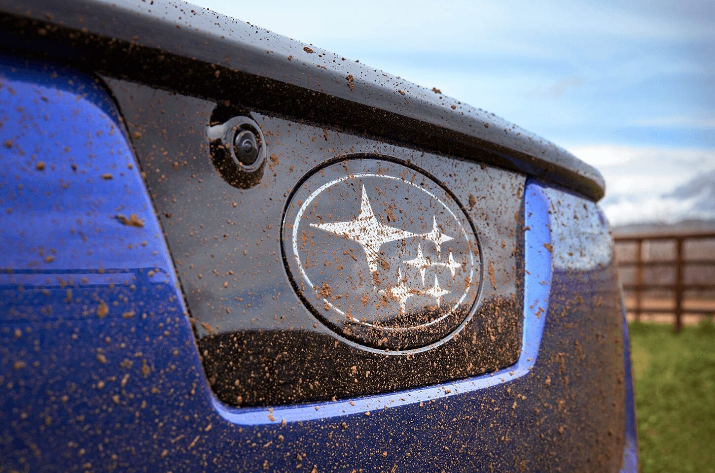 Close-up of the Subaru badge on the Trailseeker covered in mud during off-road driving.]