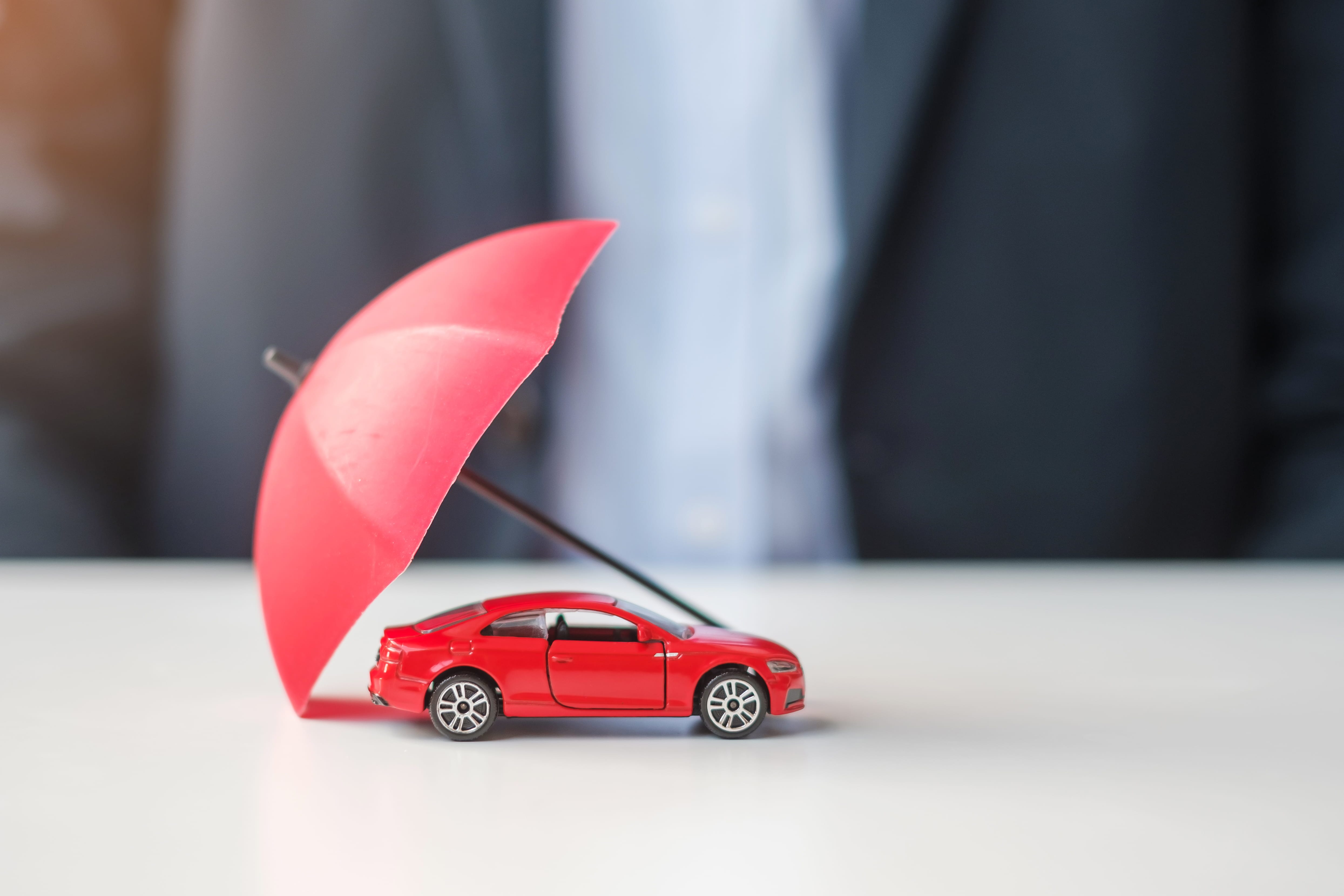 Red toy car protected by a red umbrella to represent car insurance